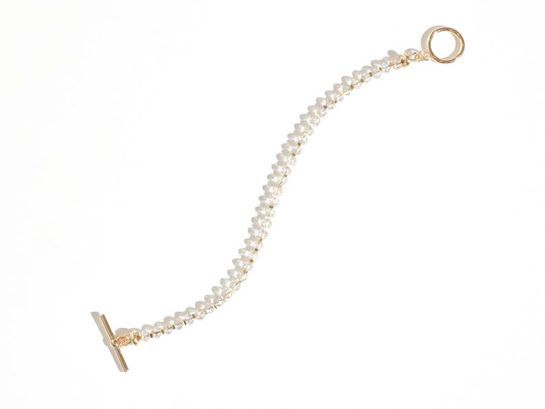 May include: A gold chain bracelet with small white beads. The bracelet has a t-bar clasp and a circular clasp.