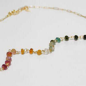 May include: A gold chain necklace with a rainbow of gemstone beads. The beads are in a zig-zag pattern and include pink, orange, yellow, white, green, and black.