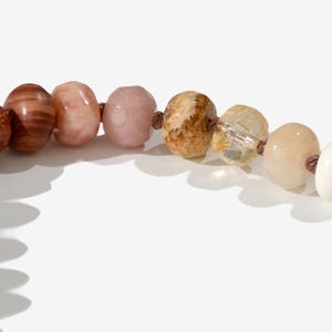 A long necklace made of various colored stones. The stones are in shades of brown, creams, white, and natural hues. The necklace has a gold clasp.