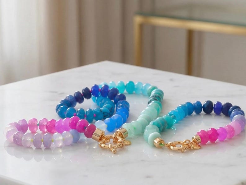 Gradient gemstone bracelet featuring genuine pink, lavender, cobalt blue, and aqua blue faceted beads with 14k gold vermeil accents and a gold toggle clasp on a white marble background.