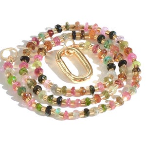 May include: A multi-colored gemstone necklace with a gold clasp. The necklace is made of small, round beads in shades of pink, green, brown, and black.