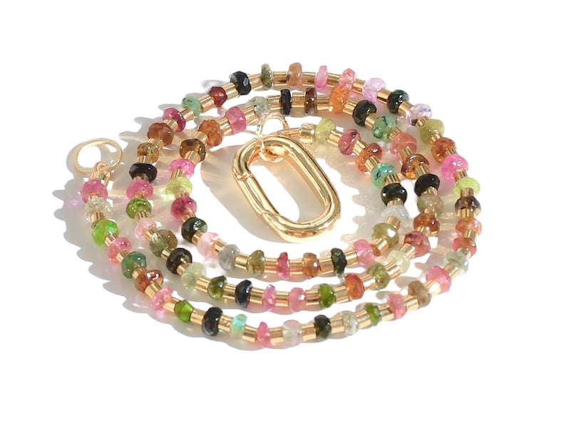May include: A multi-colored gemstone necklace with a gold clasp. The necklace is made of small, round beads in shades of pink, green, brown, and black.
