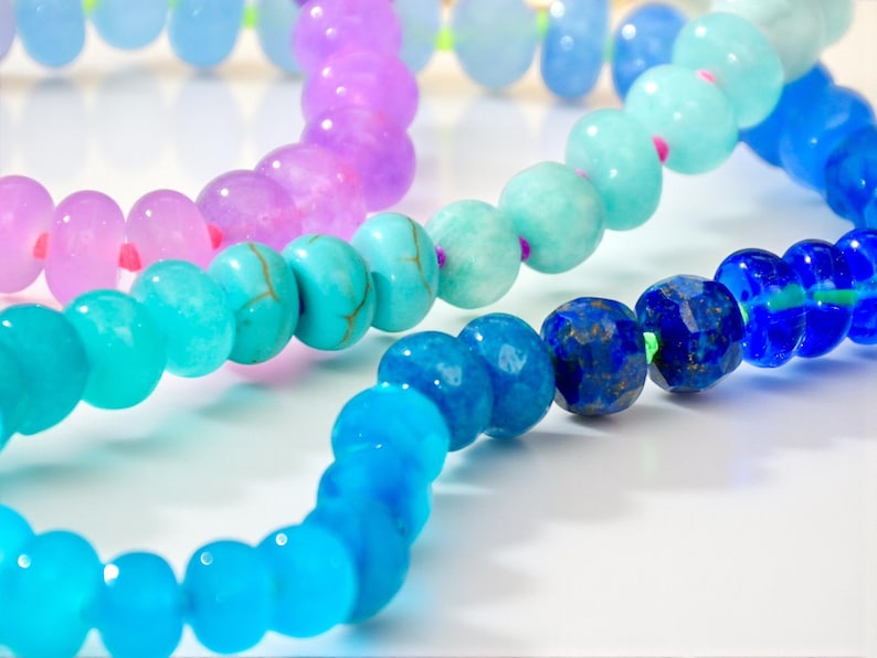 Hand-knotted gemstone necklace featuring turquoise, royal blue, and lilac beads with a gold clasp, laid out in a soft ombré gradient.