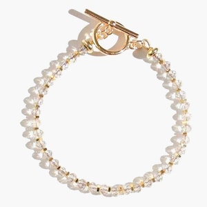 Puede incluir: Un brazalete de oro con cierre de palanca y cuentas de cristal transparente.