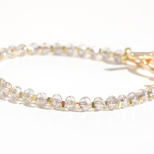 May include: A delicate gold bracelet with clear iridescent beads. The bracelet has a simple clasp closure.