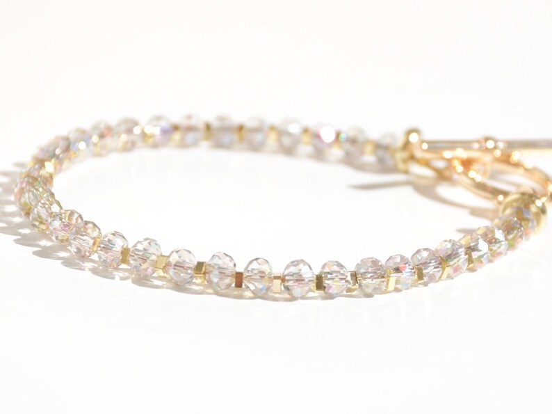May include: A delicate gold bracelet with clear iridescent beads. The bracelet has a simple clasp closure.