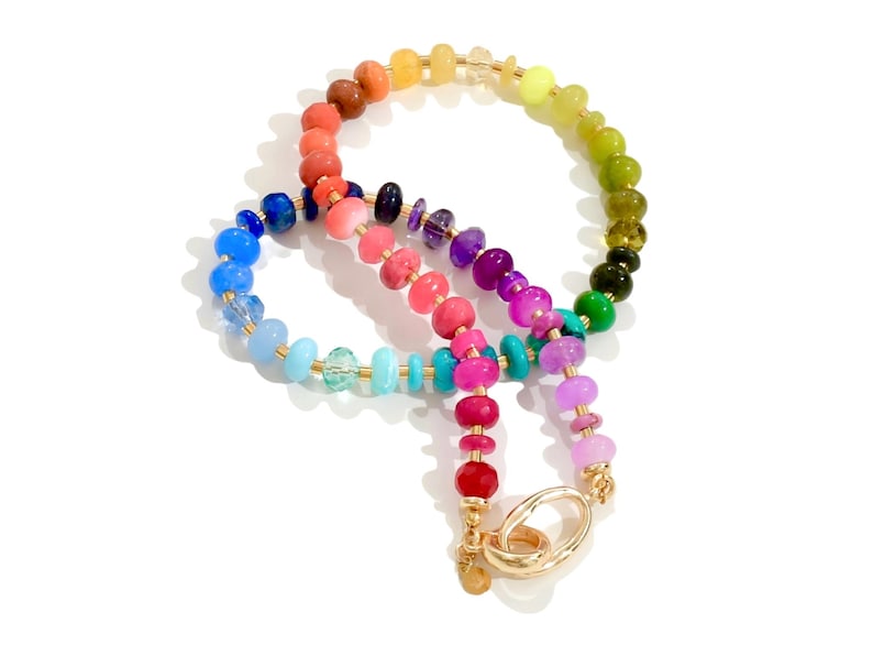 Colorful rainbow gemstone necklace featuring faceted natural stones in bold, vibrant hues with gold accents and a toggle clasp. Handmade statement jewelry displayed on a vanity with soft lighting, highlighting the sparkle and rich texture of each bead. Perfect for stacking or wearing solo.