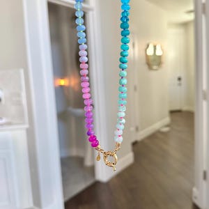Hand-knotted gemstone necklace featuring turquoise, royal blue, and lilac beads with a gold clasp, laid out in a soft ombré gradient.