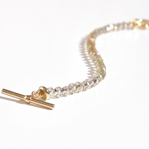 May include: A gold-toned bracelet with a T-bar clasp and iridescent clear beads.