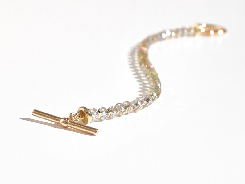 May include: A gold-toned bracelet with a T-bar clasp and iridescent clear beads.