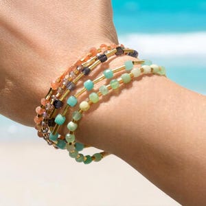 May include: A stack of colorful beaded bracelets with gold accents. The bracelets are made with different shades of green, blue, and orange beads.