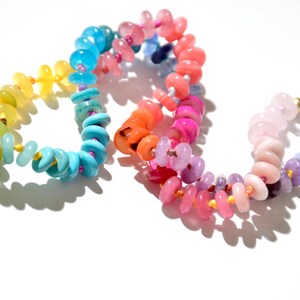May include: A rainbow colored beaded necklace with round, flat beads. The beads are arranged in a gradient pattern, starting with green and ending with purple.