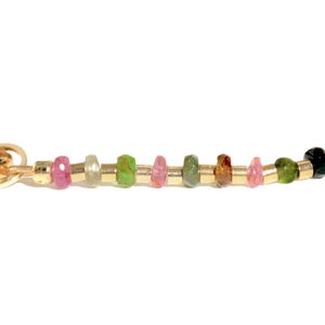 May include: A gold chain bracelet with a variety of colorful gemstones, including pink, green, brown, and black.