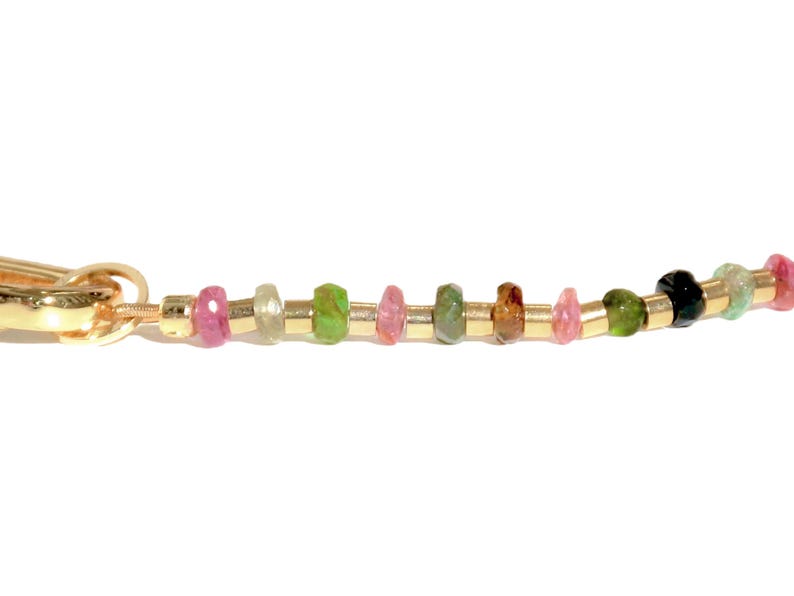 May include: A gold chain bracelet with a variety of colorful gemstones, including pink, green, brown, and black.