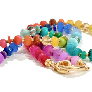 Colorful rainbow gemstone necklace and bracelet set featuring faceted natural stones in bold, vibrant hues with gold accents and a toggle clasp. Handmade statement jewelry displayed on a vanity with soft lighting, highlighting the sparkle and rich texture of each bead. Perfect for stacking or wearing solo.