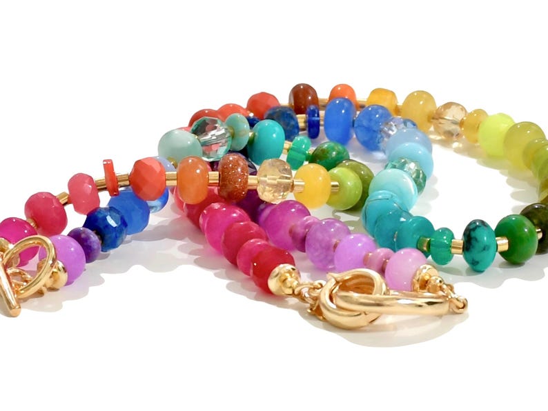 Colorful rainbow gemstone necklace and bracelet set featuring faceted natural stones in bold, vibrant hues with gold accents and a toggle clasp. Handmade statement jewelry displayed on a vanity with soft lighting, highlighting the sparkle and rich texture of each bead. Perfect for stacking or wearing solo.