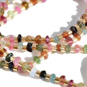 May include: A multi-strand necklace with gold beads and faceted gemstones in various colors, including pink, green, blue, and brown.