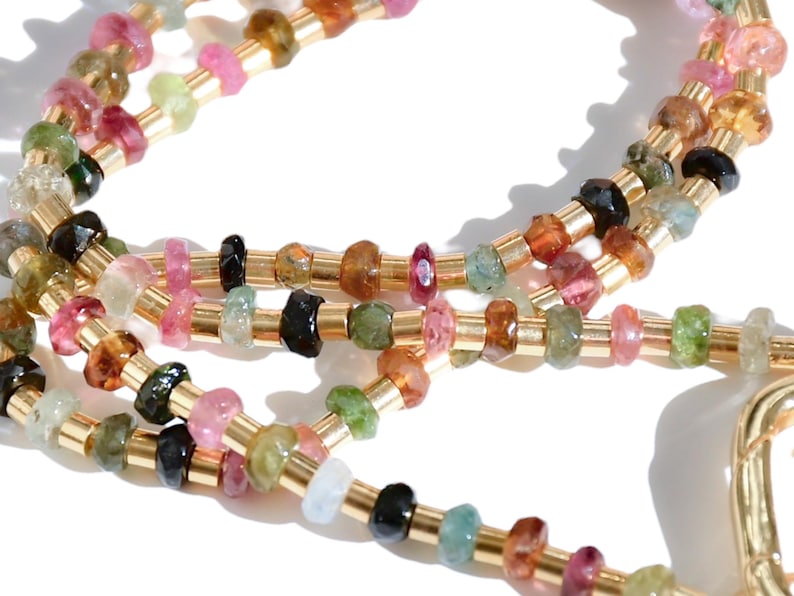 May include: A multi-strand necklace with gold beads and faceted gemstones in various colors, including pink, green, blue, and brown.
