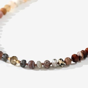 A long necklace made of various colored stones. The stones are in shades of brown, creams, white, and natural hues. The necklace has a gold clasp.
