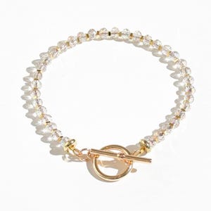 May include: A delicate gold bracelet with a toggle clasp, featuring clear crystal beads.