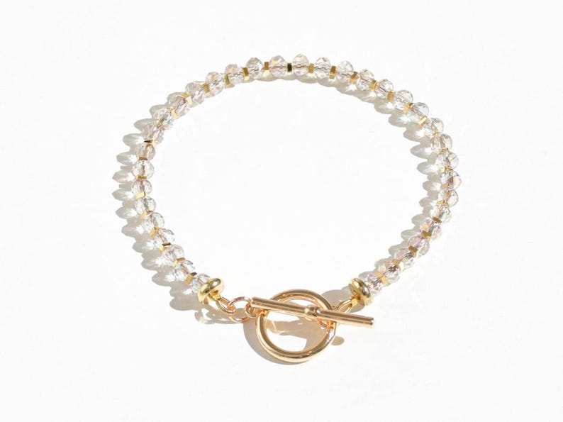May include: A delicate gold bracelet with a toggle clasp, featuring clear crystal beads.