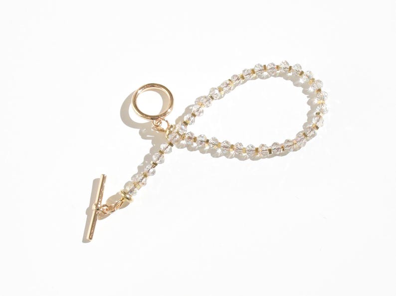 May include: A gold chain bracelet with clear crystal beads and a gold toggle clasp.