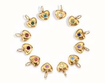 May include: A collection of gold heart-shaped pendants, each with a different colored gemstone in the center. The gemstones include blue, green, red, purple, pink, and clear stones. The pendants are arranged in a circle.