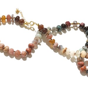 A long necklace made of various colored stones. The stones are in shades of brown, creams, white, and natural hues. The necklace has a gold clasp.