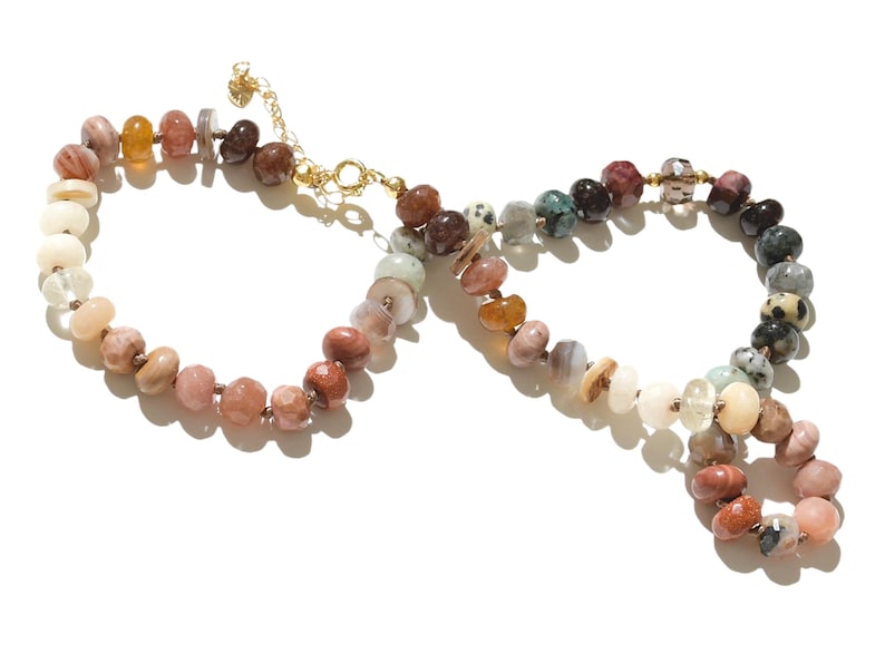 A long necklace made of various colored stones. The stones are in shades of brown, creams, white, and natural hues. The necklace has a gold clasp.