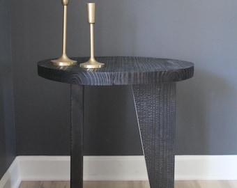 May include: A black wooden side table with a round top and three legs. Two gold candle holders are on the table.