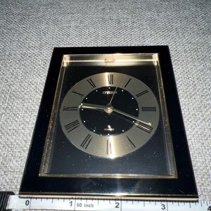 May include: A black and gold framed clock with Roman numeral markings and a black face. The clock says "Citizen Quartz" on the face.