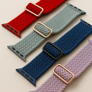 Könnte beinhalten: Nahaufnahme von fünf geflochtenen Uhrenarmbändern in Rot, Grau, Marineblau und Lavendel. Jedes Armband hat einen farblich passenden Stecker und eine rechteckige Schnalle in Gold oder Schwarz. Die Armbänder sind für eine Smartwatch konzipiert.
