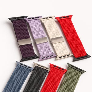 Può includere: Una selezione di cinturini per orologi elasticizzati intrecciati in vari colori, tra cui viola, lavanda, crema e rosso. I cinturini hanno chiusure in metallo e sono progettati per smartwatch. Presentati su sfondo bianco.