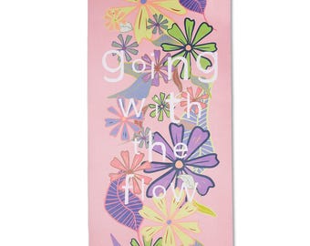 May include: A pink yoga mat featuring a floral pattern in yellow, green, purple, and pink. The words "going with the flow" are printed vertically in white. The mat is rectangular in shape.