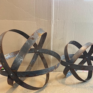 May include: Two metal sphere sculptures made of rusty metal rings. The larger sphere is in the foreground and the smaller sphere is in the background.