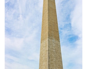 May include: A tall, stone monument with a pointed top, known as the Washington Monument, stands against a blue sky with white clouds.  American flags line the ground in front of the monument. The text "@filmcityprints" is visible in the lower center of the image.