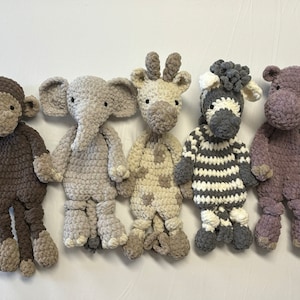 Puede incluir: Un conjunto de cinco animales de peluche tejidos a ganchillo que incluye un mono marrón oscuro, un elefante gris claro, una jirafa crema y beige, una cebra a rayas blancas y negras y un hipopótamo morado, todos con texturas de hilo suave.