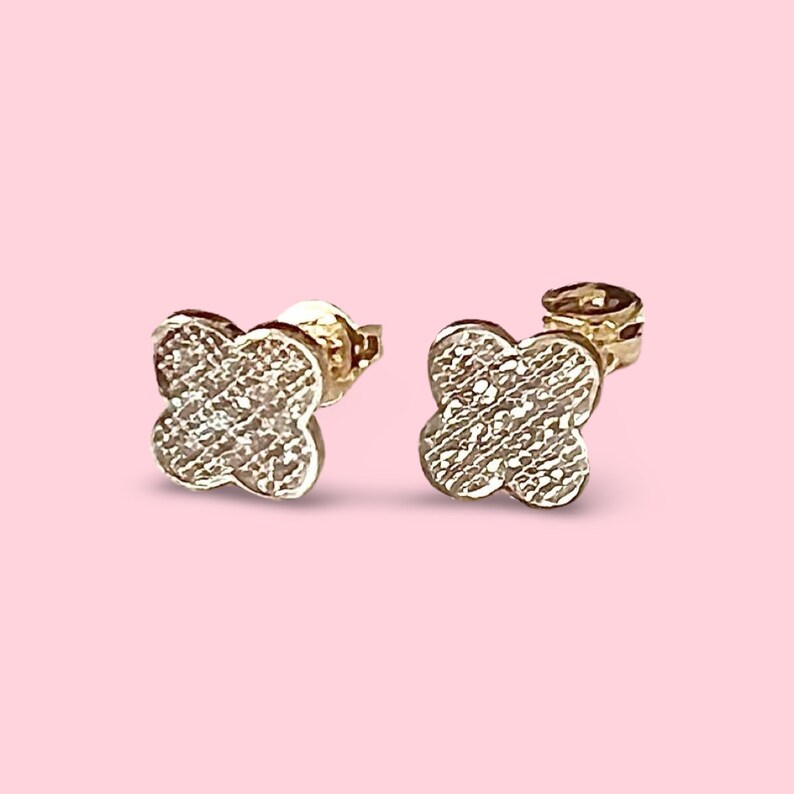 Puede incluir: Un par de pendientes de tr&eacute;bol de oro con peque&ntilde;as piedras transparentes engastadas en el metal. Los pendientes tienen un poste y una mariposa en la parte posterior.