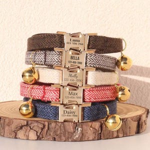 May include: A stack of personalized pet collars with gold-colored buckles and bells. The collars are in various colors and patterns, including brown, white, red, and blue herringbone designs. Each buckle is engraved with a pet's name and a phone number.