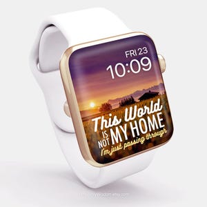 May include: A white Apple Watch with a gold band and a sunset-themed watch face. The watch face displays the time as 10:09 and the date as FRI 23. The watch face also includes the text "This world is not my home I'm just passing through".