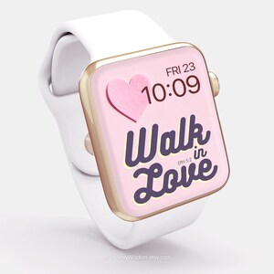Op de afbeelding: Een witte Apple Watch met een gouden band en een roze wijzerplaat. De wijzerplaat toont de tijd, "FRI 23 10:09", en de tekst "Walk in Love" met de bijbelverwijzing "EPH 5:2". Een roze papieren hart bevindt zich in de linkerbovenhoek van de wijzerplaat.