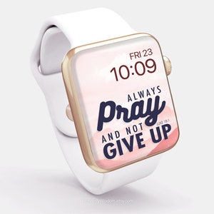 Op de afbeelding: Een witte Apple Watch met een gouden band en een roze en witte aquarel achtergrond. Het horloge gezicht toont de tijd 10:09 en de tekst "Altijd bidden en niet opgeven" met de Bijbelvers Lukas 18:1.