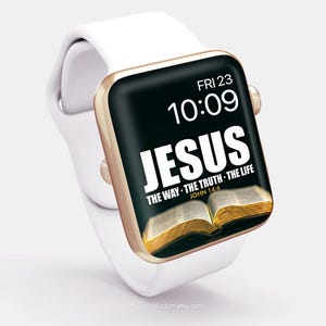 Op de afbeelding: Een witte smartwatch met een goudkleurige rand toont het woord "JESUS" in grote witte letters op een zwarte achtergrond. Het scherm toont ook de tijd, datum en een bijbelvers. Het horloge heeft een witte band.