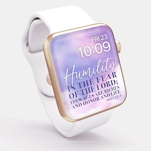 Könnte beinhalten: Eine weiße Apple Watch mit goldenem Armband und einem lila und rosafarbenen Aquarellhintergrund. Das Zifferblatt der Uhr zeigt die Zeit "FRI 23 10:09" und den Text "Humility is the fear of the Lord; its wages are riches and honour and life Prov 22:4".
