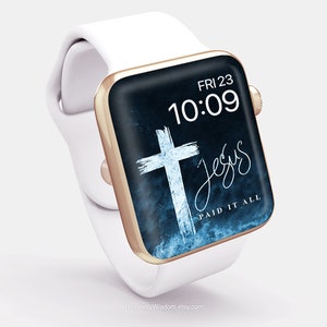Op de afbeelding: Een witte Apple Watch met een gouden rand en een blauw en zwart wijzerplaat. De wijzerplaat heeft een wit kruis op een blauwe achtergrond en de tekst "Jesus Paid It All". De tijd is 10:09 en de datum is FRI 23.