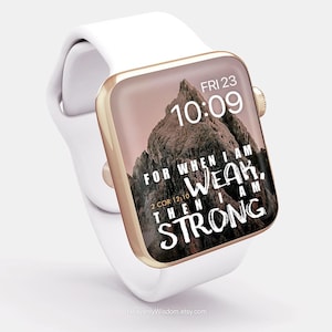 Op de afbeelding: Een witte smartwatch met een goudkleurige rand toont de tijd en een bergbeeld met de tekst "FOR WHEN I AM WEAK, THEN I AM STRONG" en "2 COR 12:10". De horlogeband is wit.