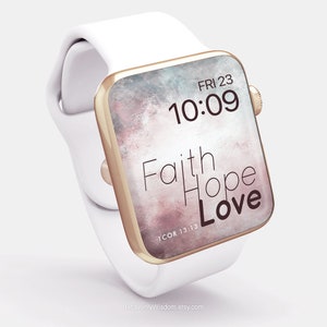 Op de afbeelding: Een witte Apple Watch met een roségouden band en een digitaal klokje dat "FRI 23 10:09" aangeeft. De wijzerplaat heeft een aquarel achtergrond met de woorden "Faith Hope Love" en de bijbelverwijzing "1 COR 13:13".