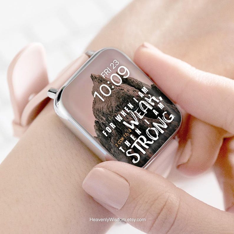 May include: A rose-colored smartwatch with a silver frame displays the time, "FRI 23 10:09", and a mountain graphic. The watch face also features the text "FOR WHEN I AM WEAK, THEN I AM STRONG" and "2 COR 12:10". The watch is on a wrist.