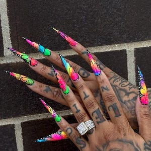 Könnte beinhalten: Lange, stiletto-förmige künstliche Fingernägel mit einem leuchtenden Schmetterlingsflügelmuster in neonfarbenen Pink-, Gelb-, Blau- und Grüntönen. Das Design umfasst schwarze Umrandungen und weiße Punkte auf schwarzer Basis für einen Flügeleffekt.