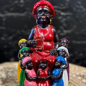 May include: A red, black, and gold statue of a woman with seven children. The woman is wearing a red dress and a red hat. The children are wearing dresses of different colors. The statue is labeled "Madama".